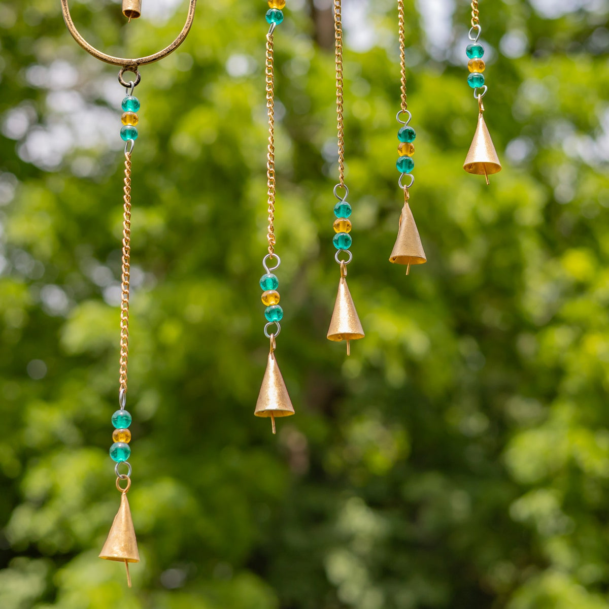 Gold-toned cone bells hang from fine chains with turquoise and amber beads against a leafy background.
