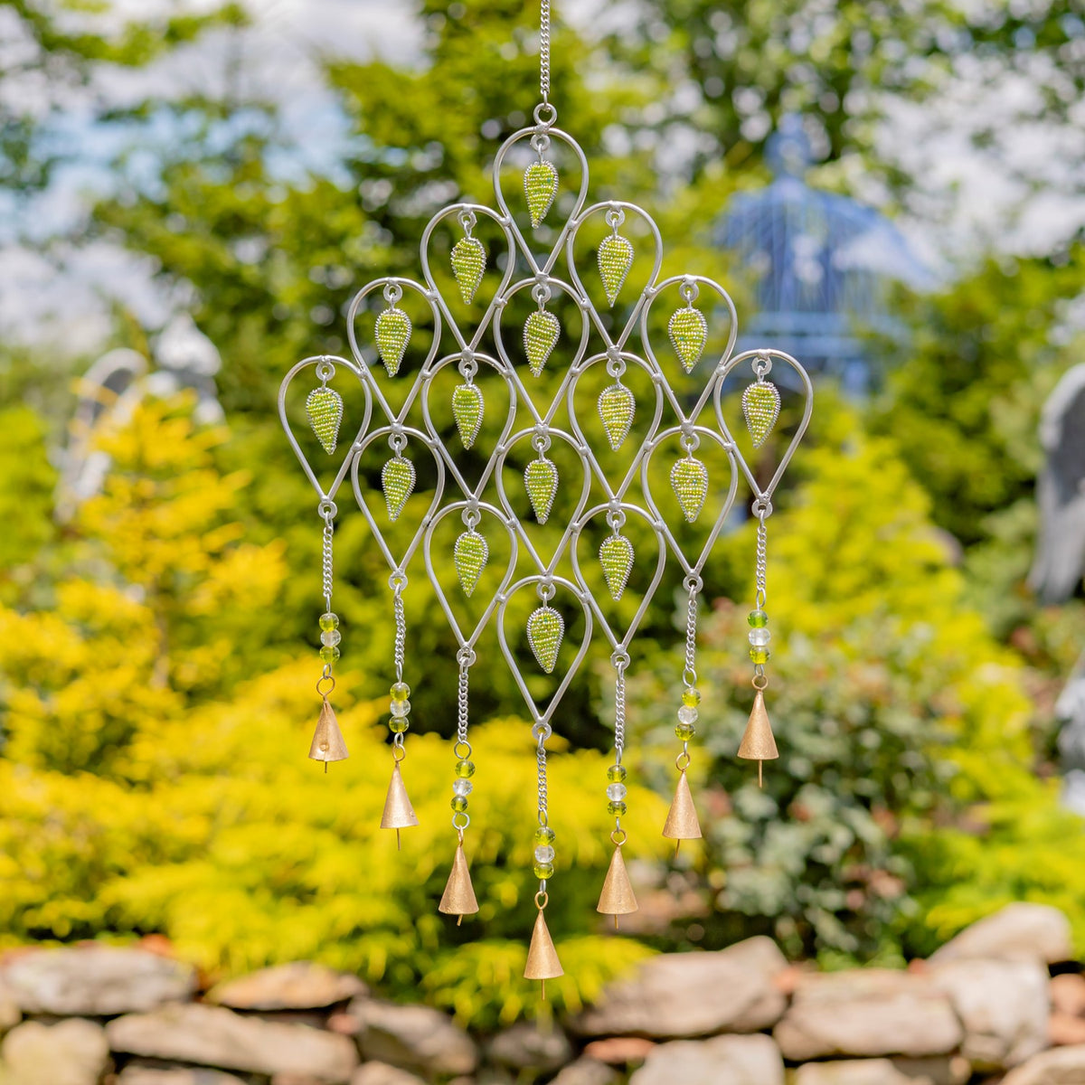 Silver metal wind chime with lime-green accents and dangling beads and bells against a leafy garden.