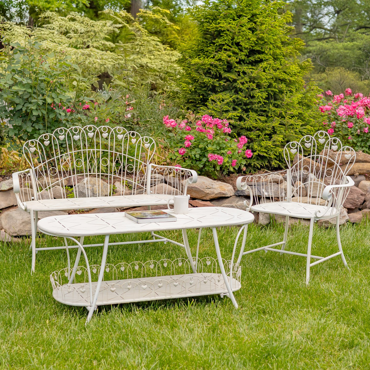 White oval garden table with a lower shelf, shown with matching chairs on a lawn.