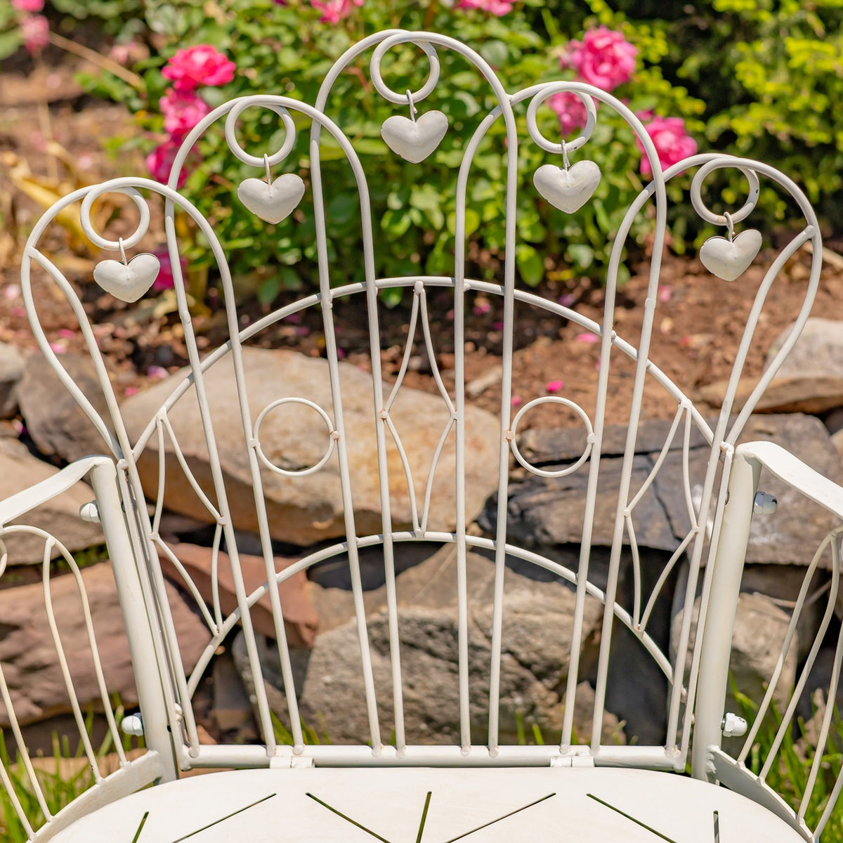 Close view of the arched metal backrest with curled loops and hanging heart-shaped accents.