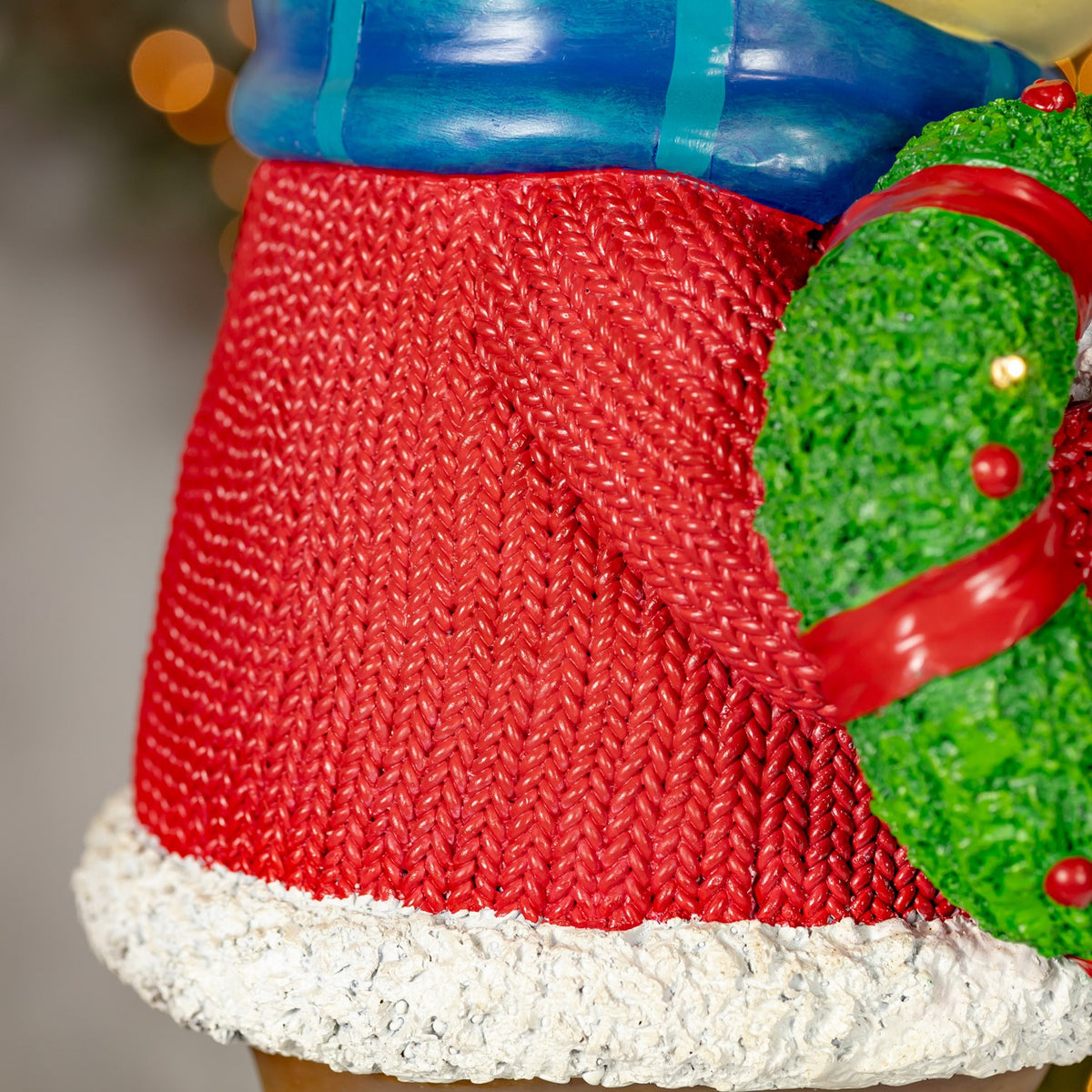 Close-up of the textured red sweater, white trim, and green wreath with a red bow.
