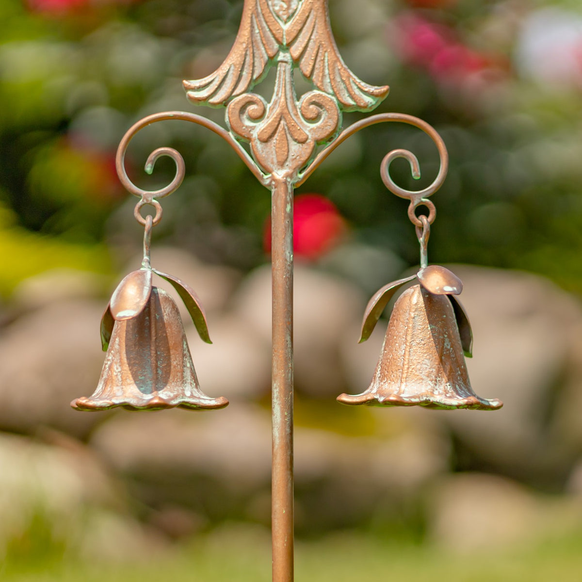 Close-up of two bell ornaments hanging from curled arms beneath an ornate metal cross.