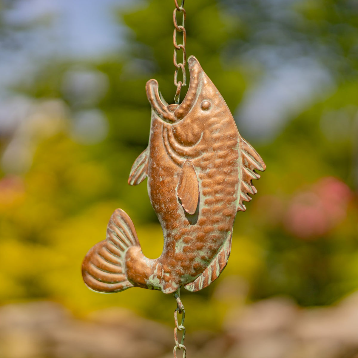 Close-up of an embossed fish-shaped rain chain link with a warm copper-colored finish.