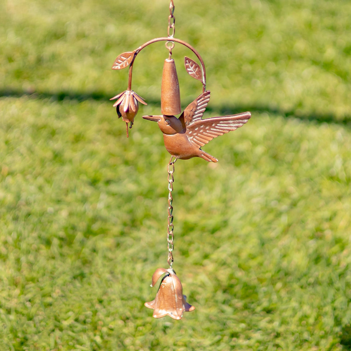 Close view of a copper-toned hummingbird beside a flower-shaped cup, with another flower hanging below.