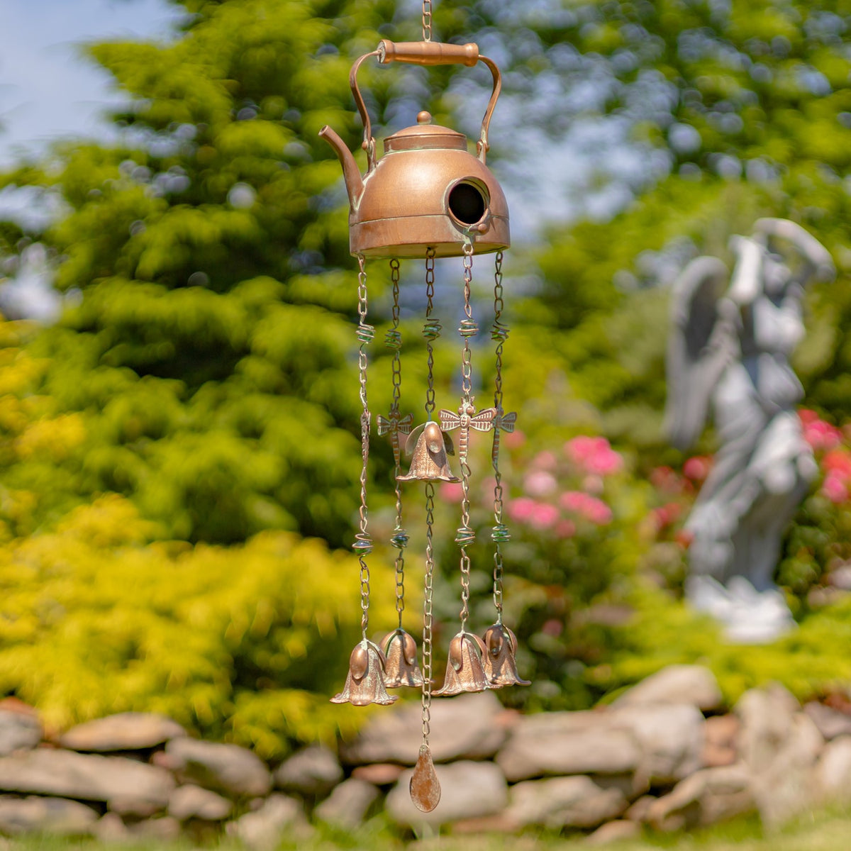 Rounded kettle-shaped birdhouse wind chime with dangling chains and bells against a leafy garden.