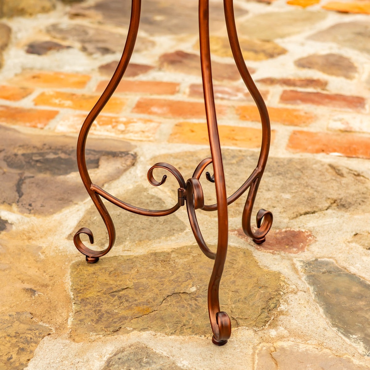 Close-up of the birdbath stand’s curved legs and curled feet on a stone patio.