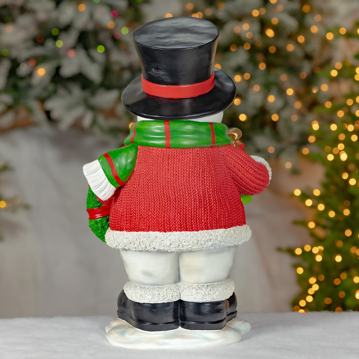 Back of the snowman wearing a red sweater, green scarf, and black top hat.