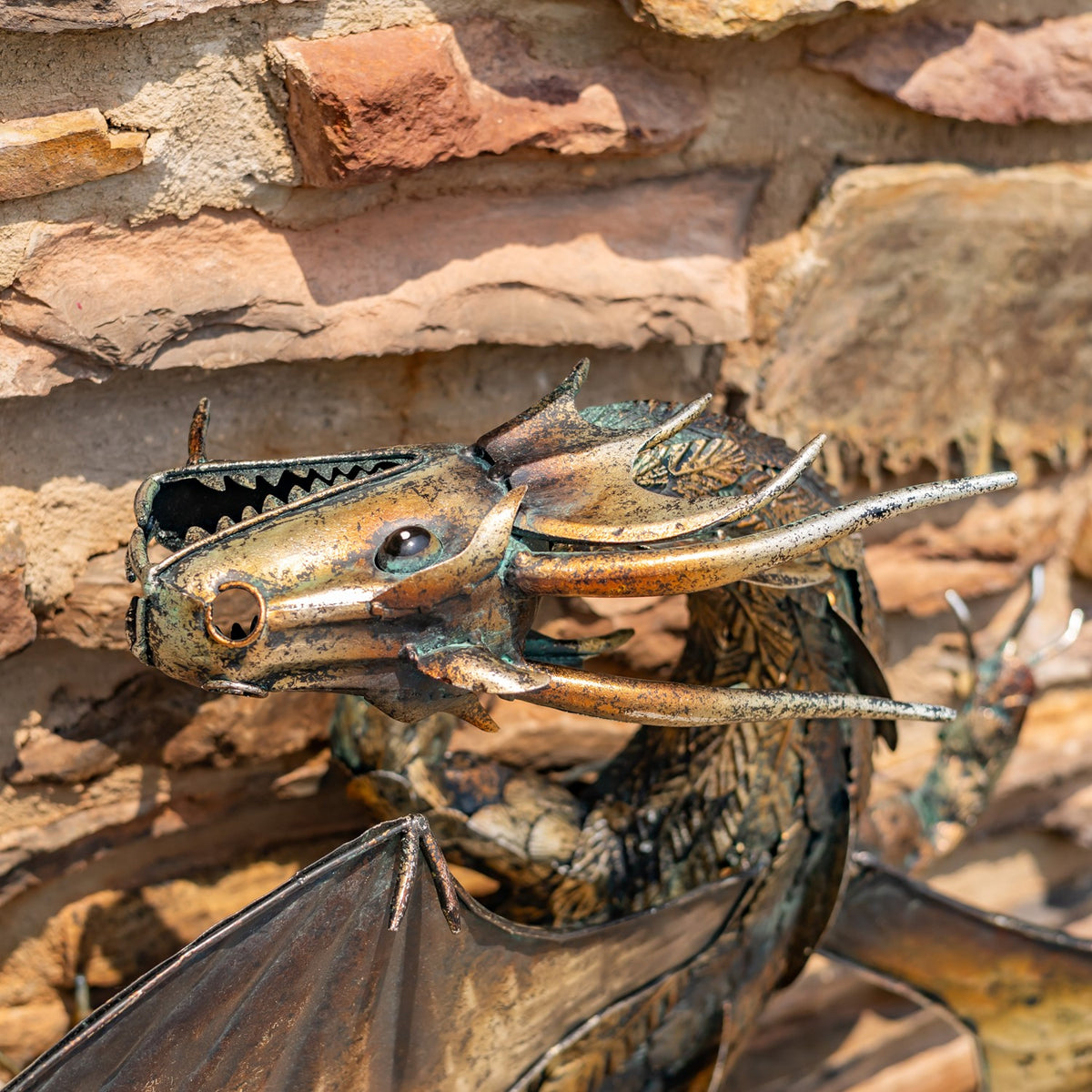 Close-up of the dragon’s horned metal head and open mouth against a stone wall.