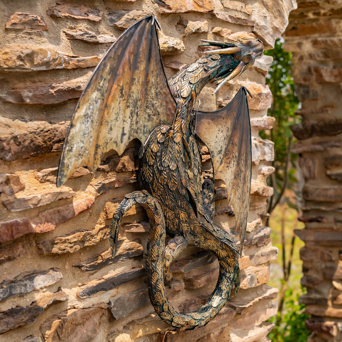 Sculpted metal dragon with spread wings and a curled tail displayed against a stacked-stone wall.
