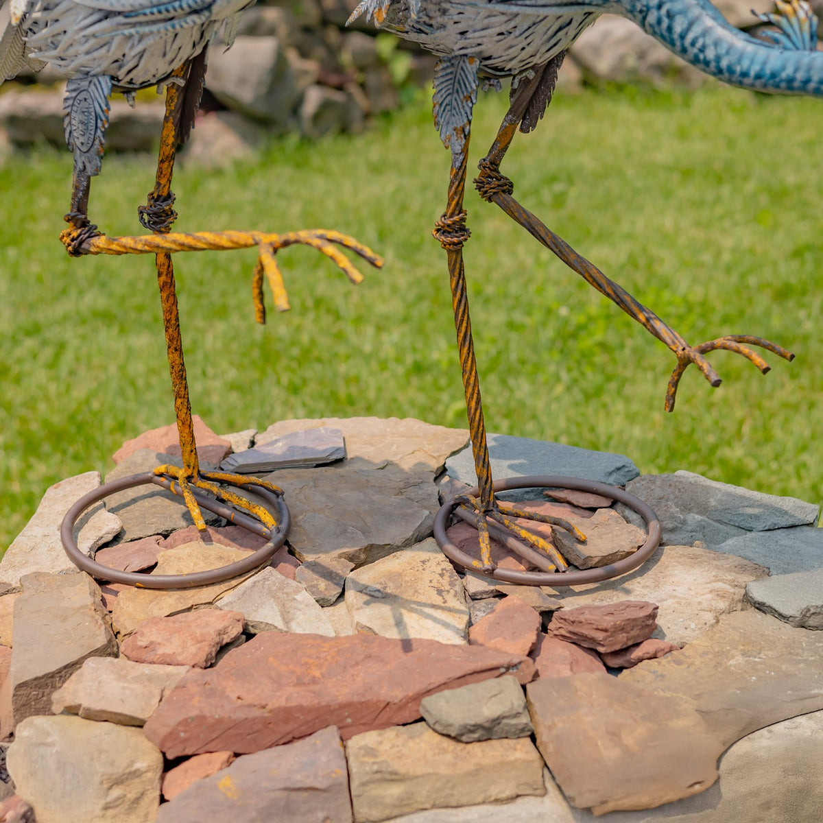Circular iron bases and legs of two heron figurines on a stone surface