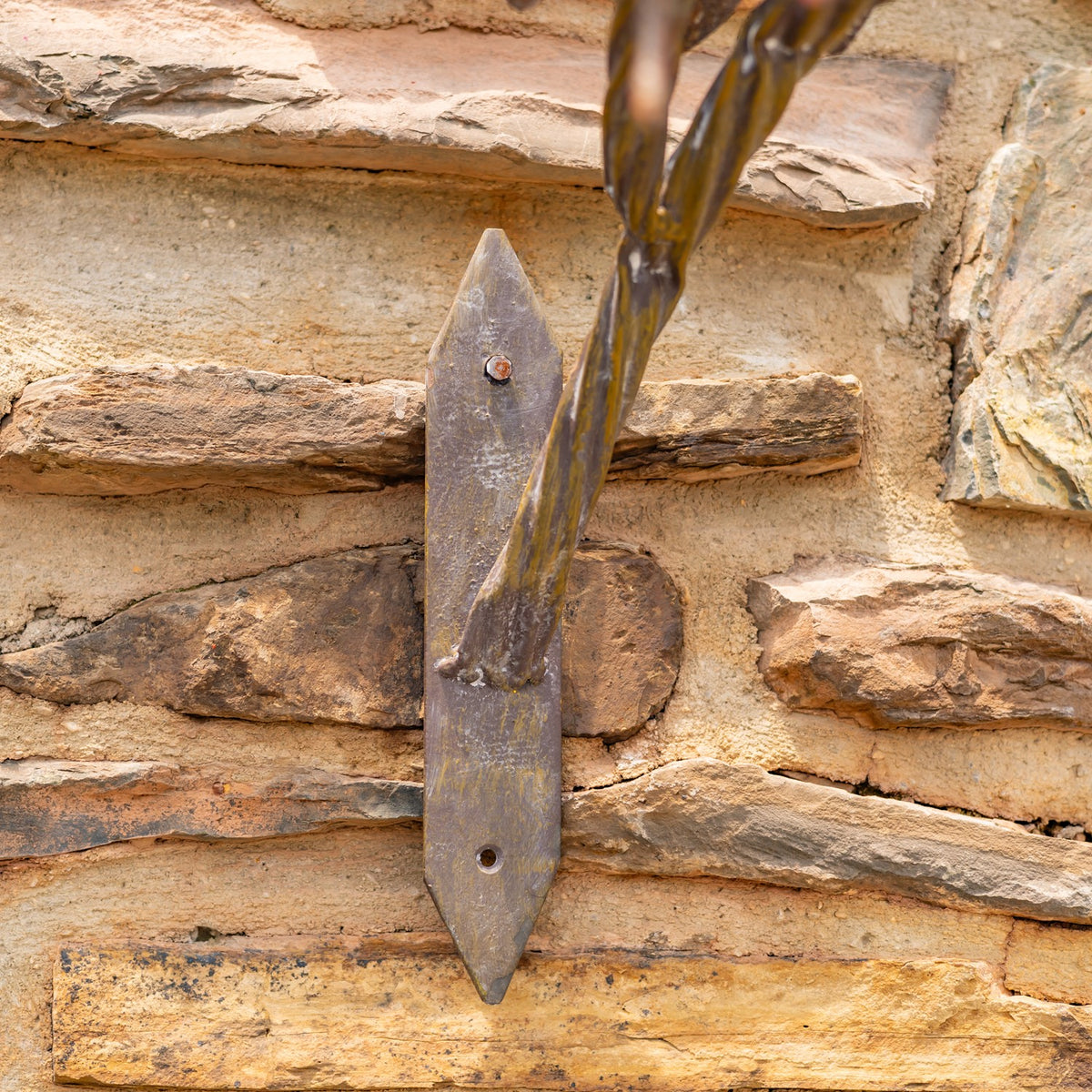 Close-up of the sculpture’s metal mounting plate and support attached to a stacked stone wall.