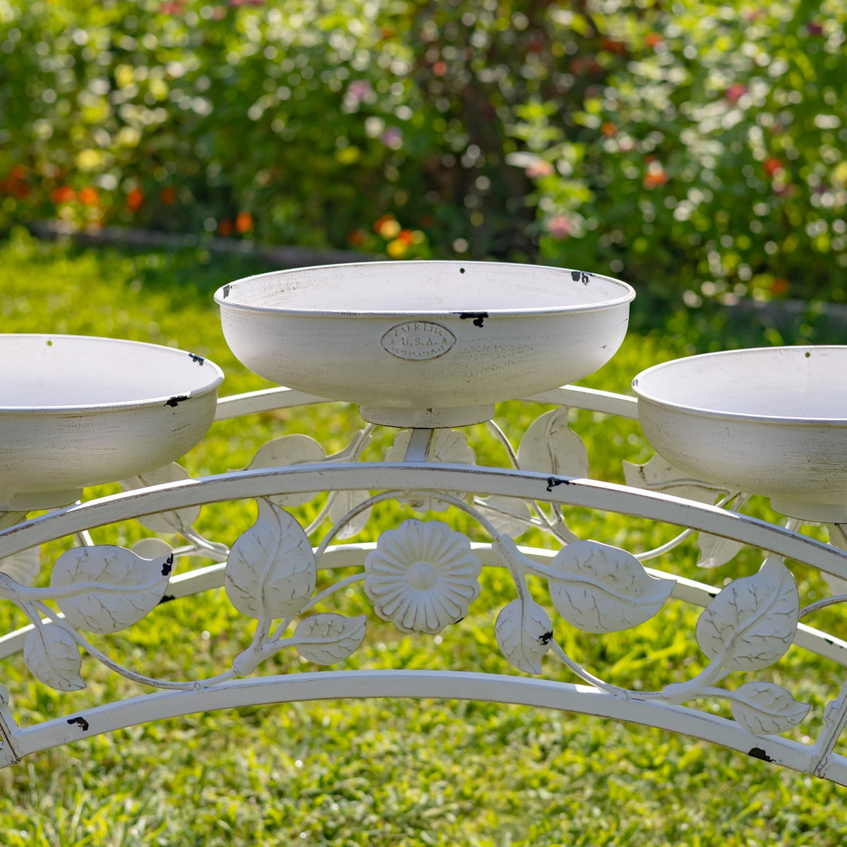 Three shallow white bowls sit above an arched rail decorated with metal leaves and a flower motif.