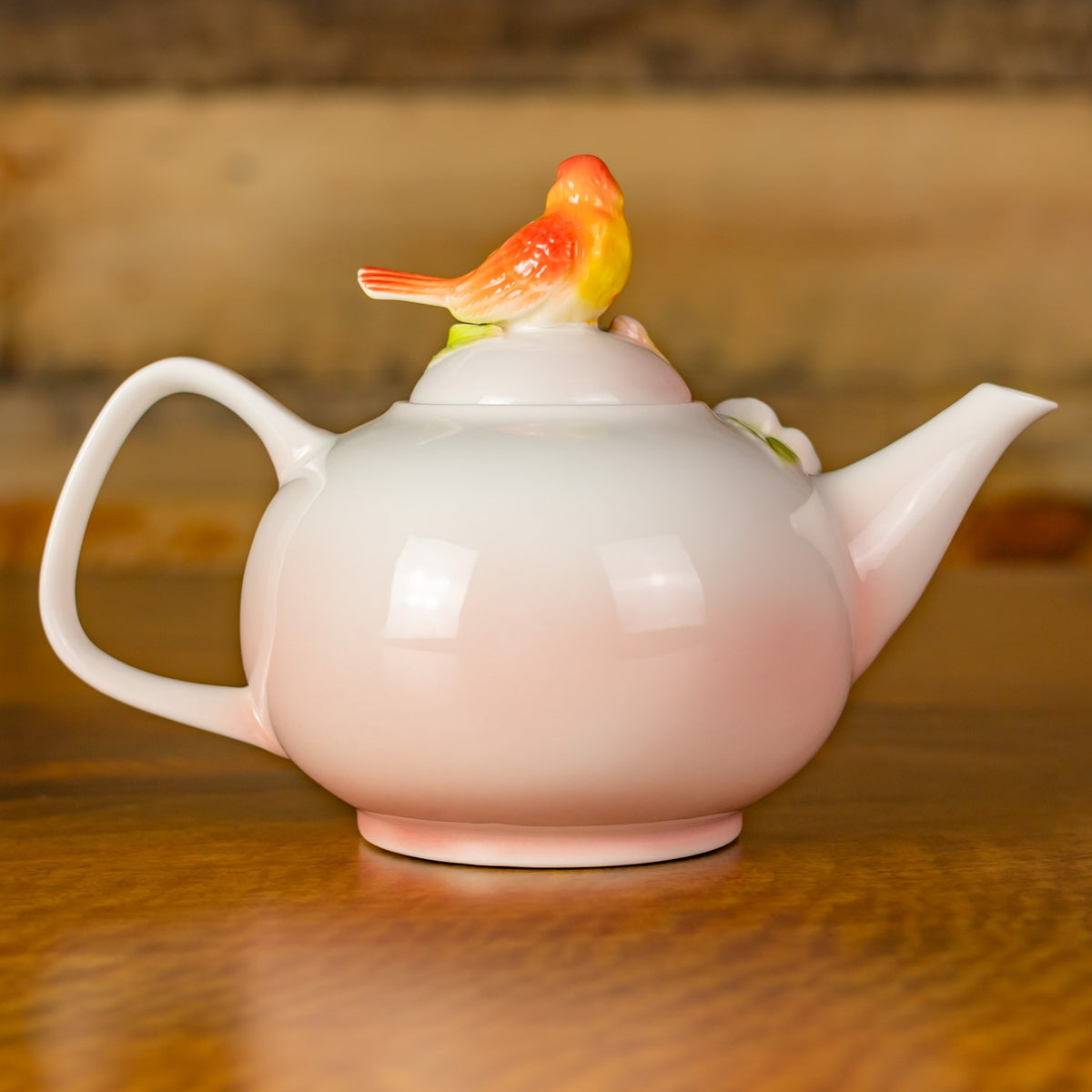 Plain white side of the teapot, with its handle, spout, and bird ornament visible against a wooden background.