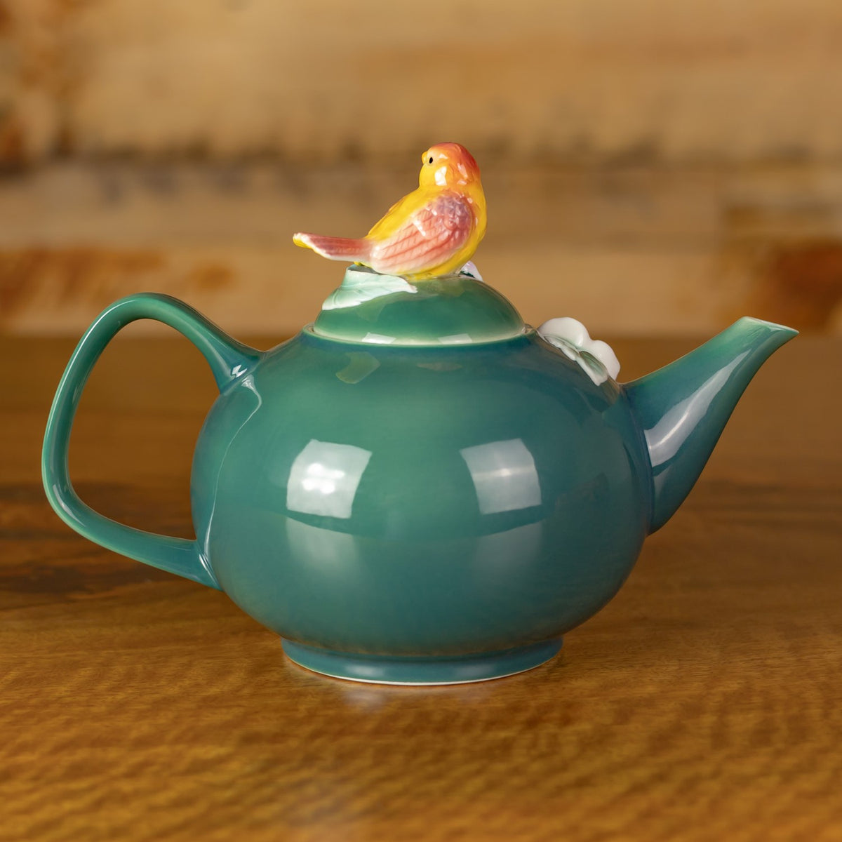 Rear of the glossy teal teapot, showing its curved handle, spout, and bird-shaped lid ornament.