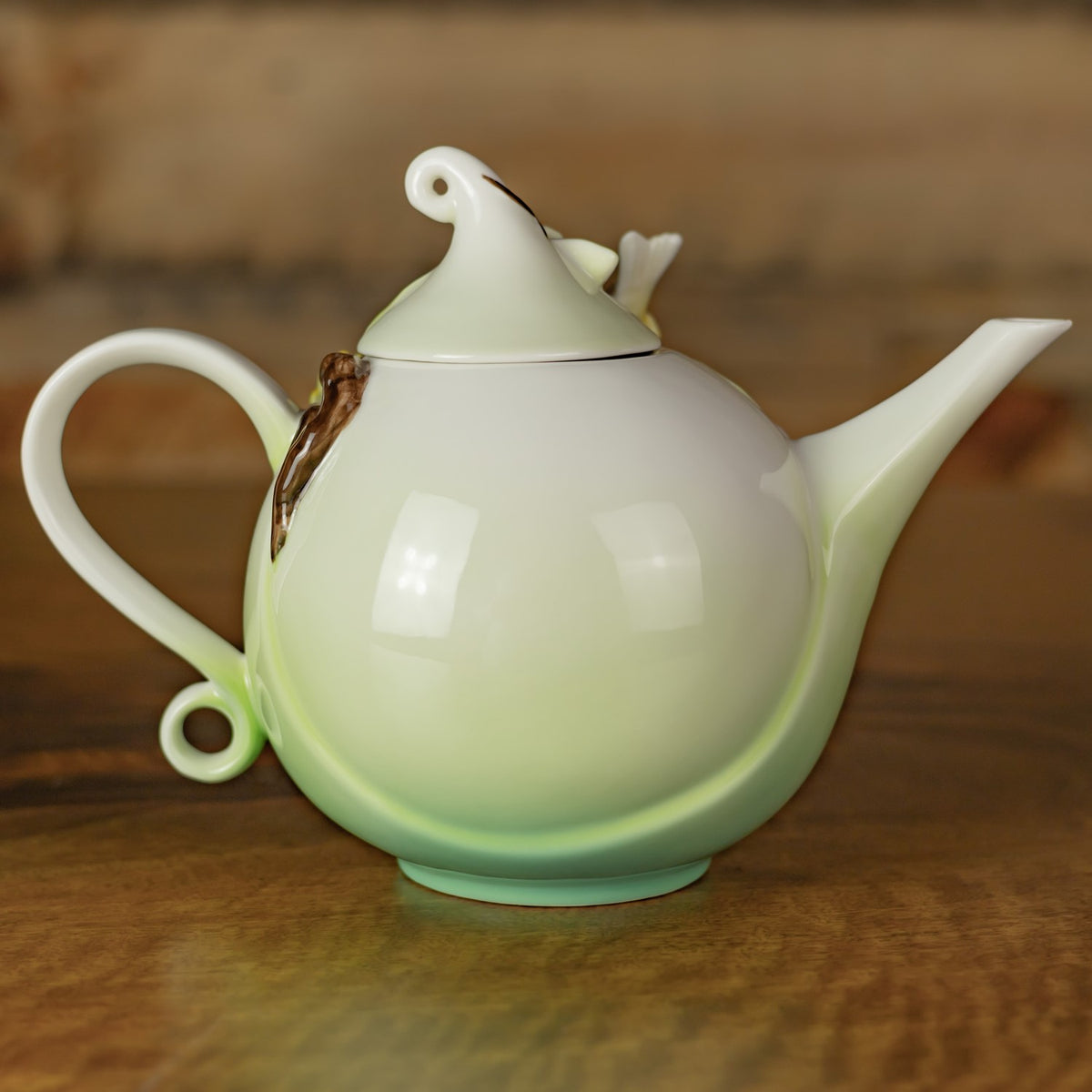 Back of the pale teapot, showing its rounded body, curled handle, long spout, and lid.