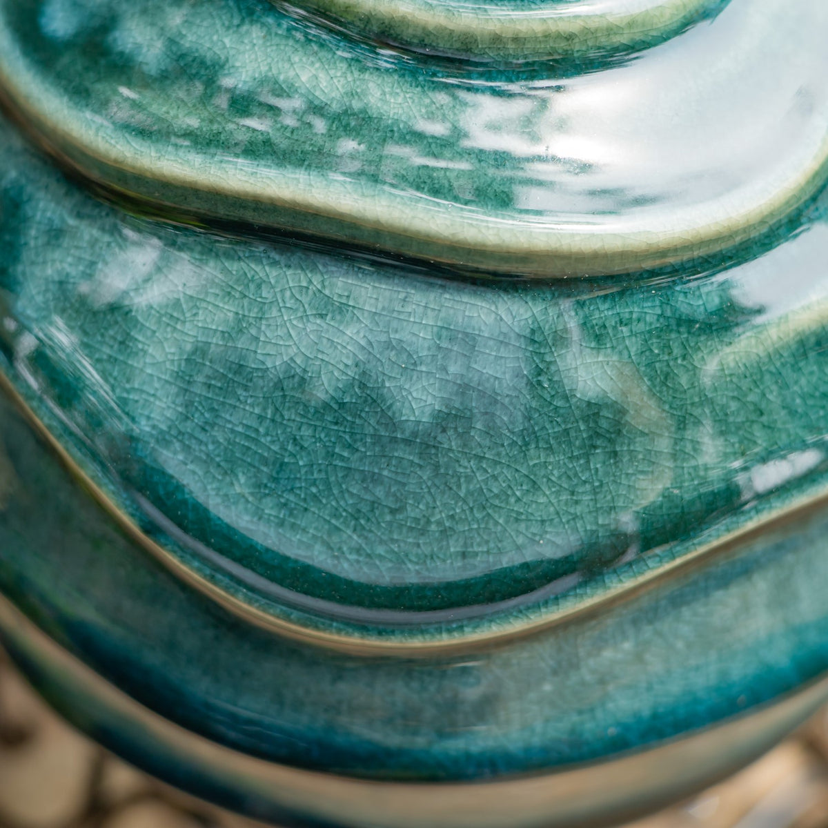 Close-up of the globe’s glossy teal glaze, showing fine crackle texture and raised curved bands.