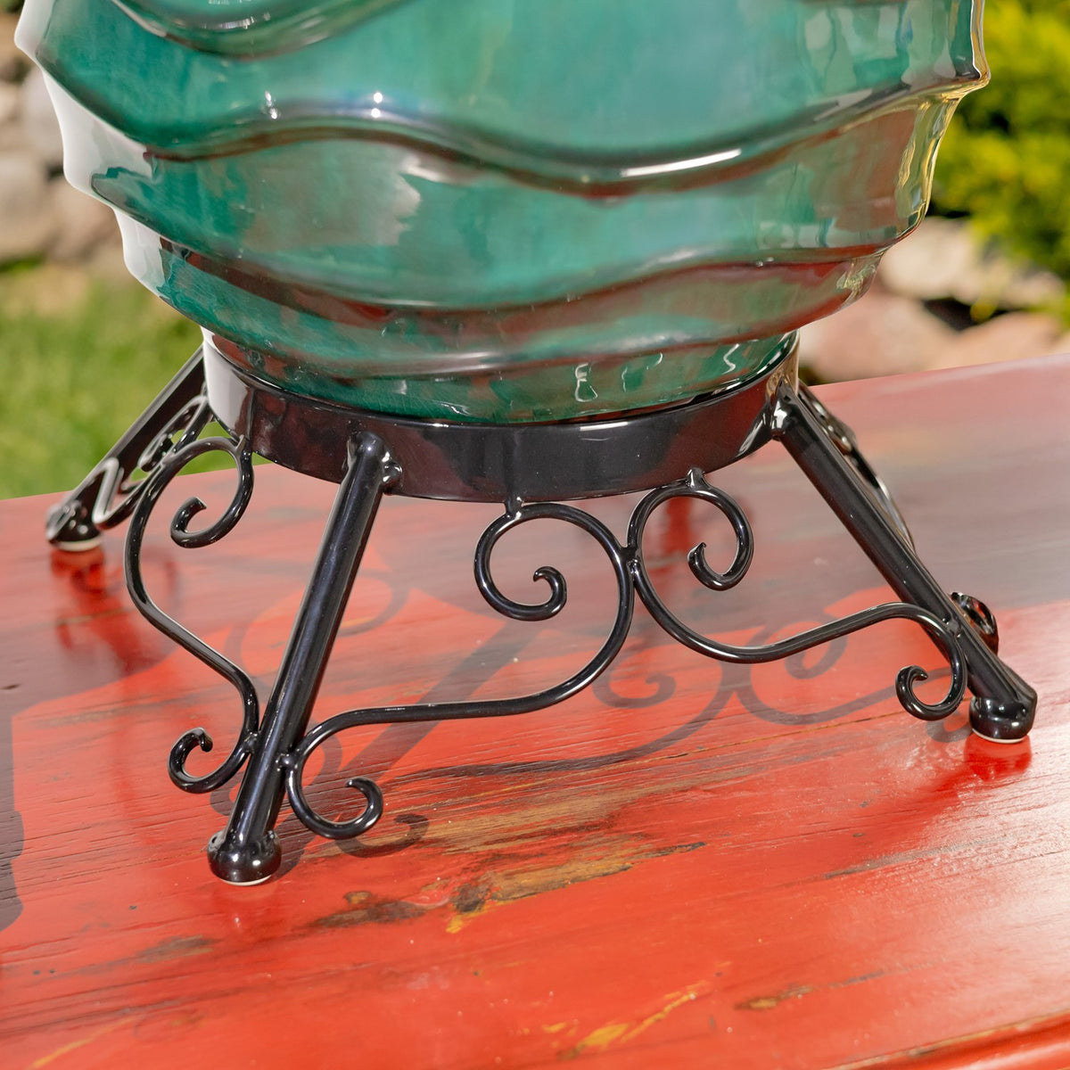 Close-up of a glossy teal globe above the curled legs of its black metal stand on a red bench.