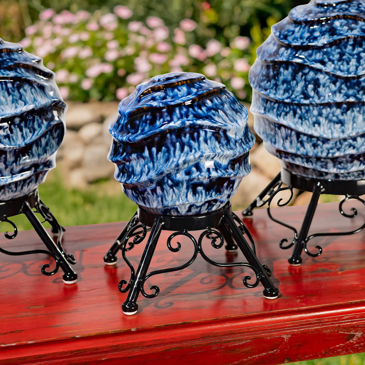 Three blue-and-white gazing globes on ornate black metal stands arranged on a red table.