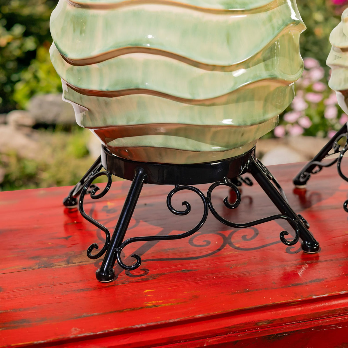 Close-up of a pale green ceramic globe above a black metal stand with curled scrollwork on a red table.