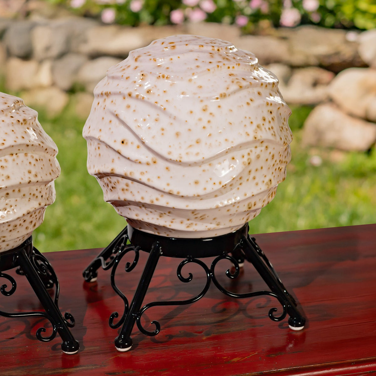 A cream speckled globe with layered wavy ridges sits on a black metal stand beside a partial second globe.