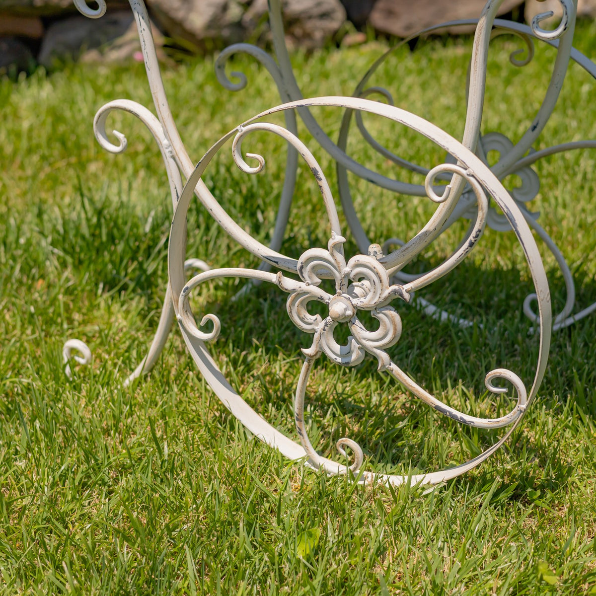 Close-up of a decorative metal wheel with curled spokes and a flower-shaped center on grass.