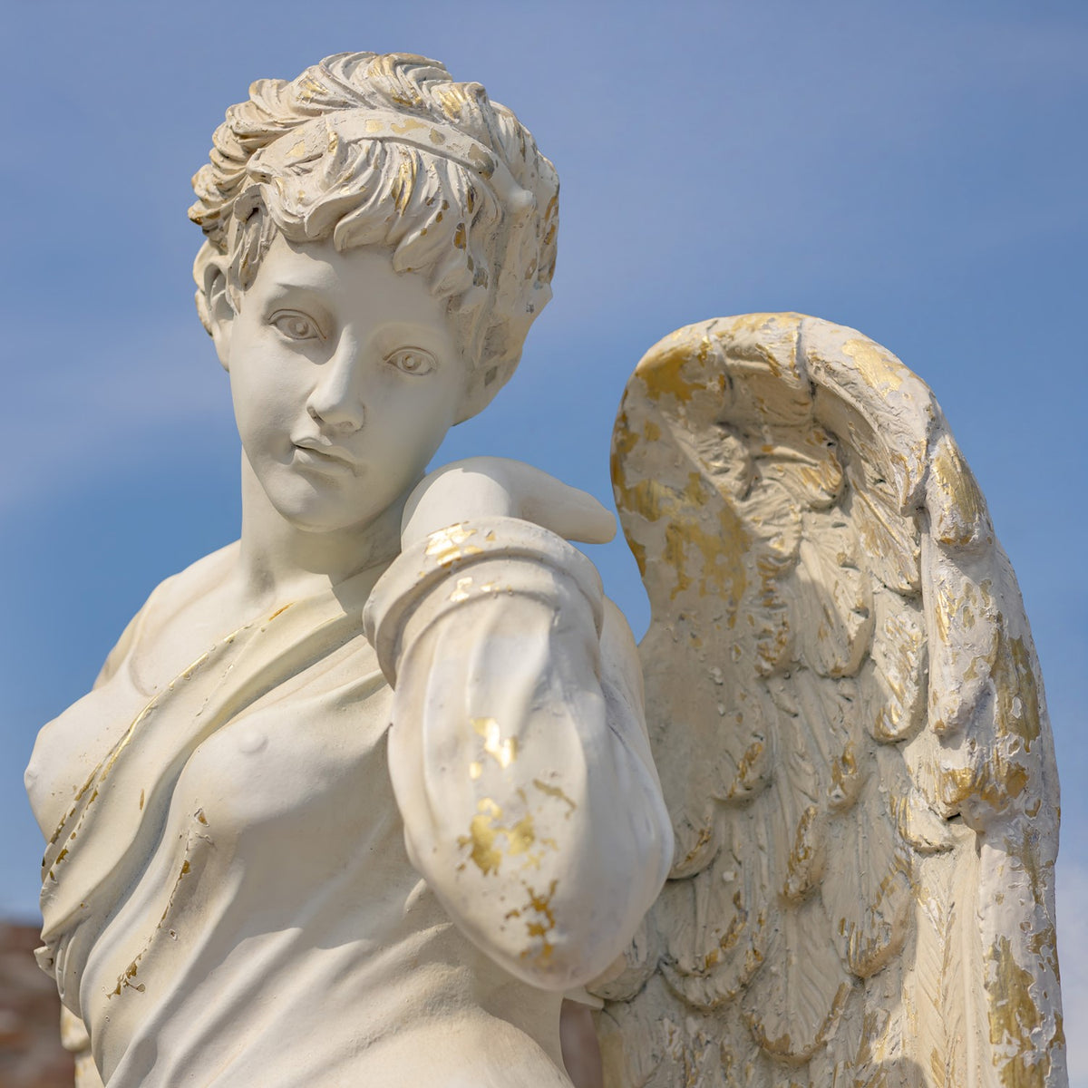 Close view of the angel’s face, curled hair, draped shoulder, and weathered wing.