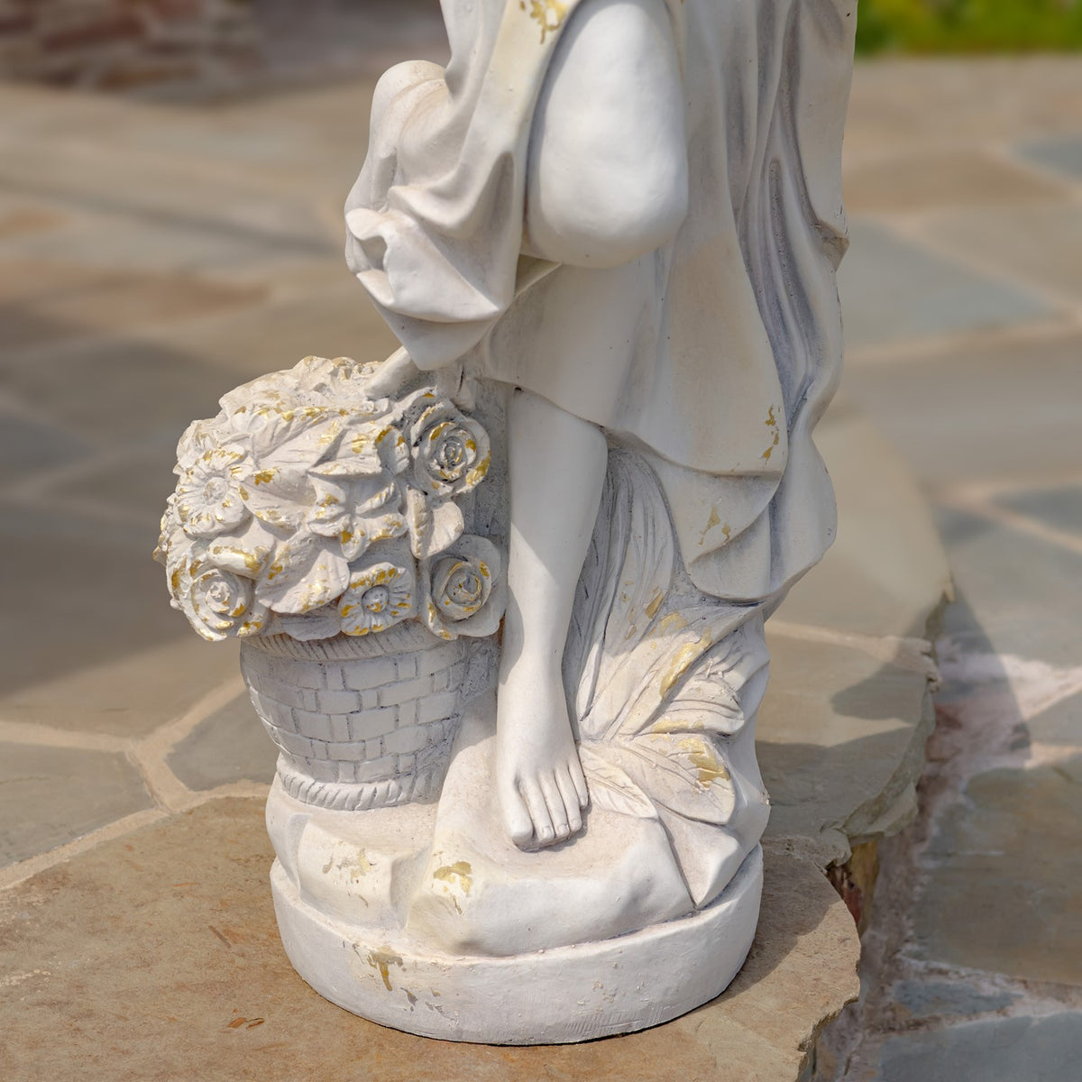 The statue’s draped lower body, bare foot, and flower basket are shown on its round base.