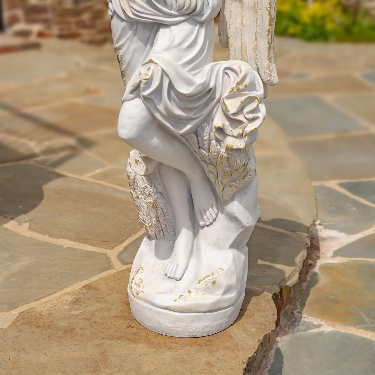 Close view of the draped robe, bare feet and round base on a stone patio.