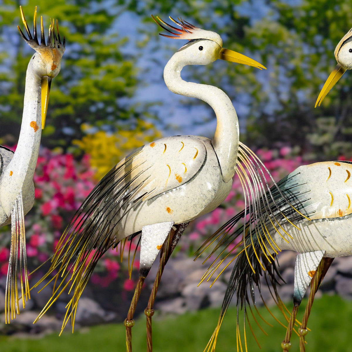 A curved-neck heron figurine stands among other birds, showing its yellow beak and long, layered metal feathers.