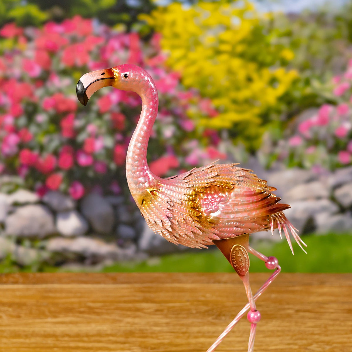 Pink metal flamingo figurine in profile, showing its curved neck, layered feathers, and one bent leg.