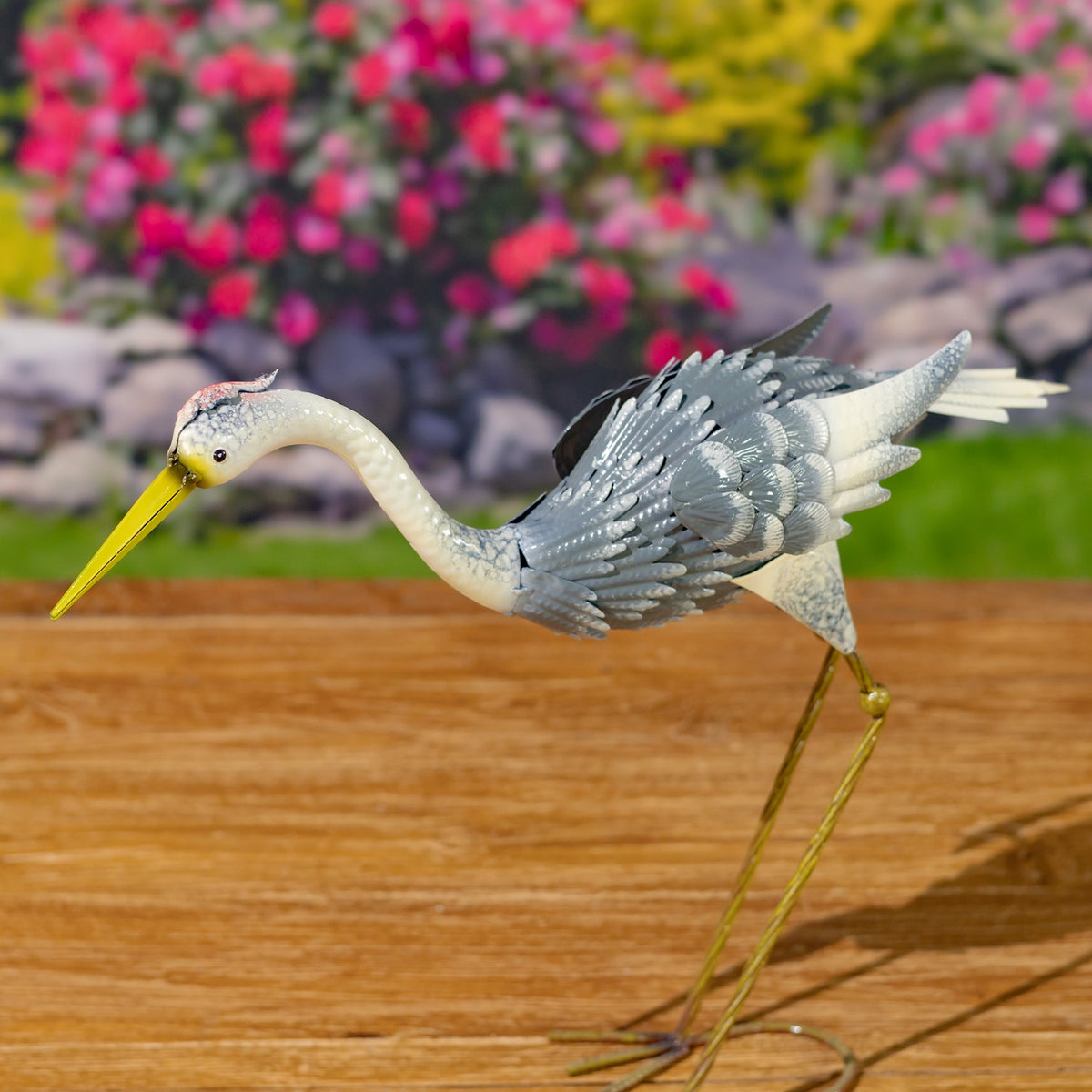 Metal heron figurine bends forward, its yellow beak pointing down and long legs extending beneath its body.