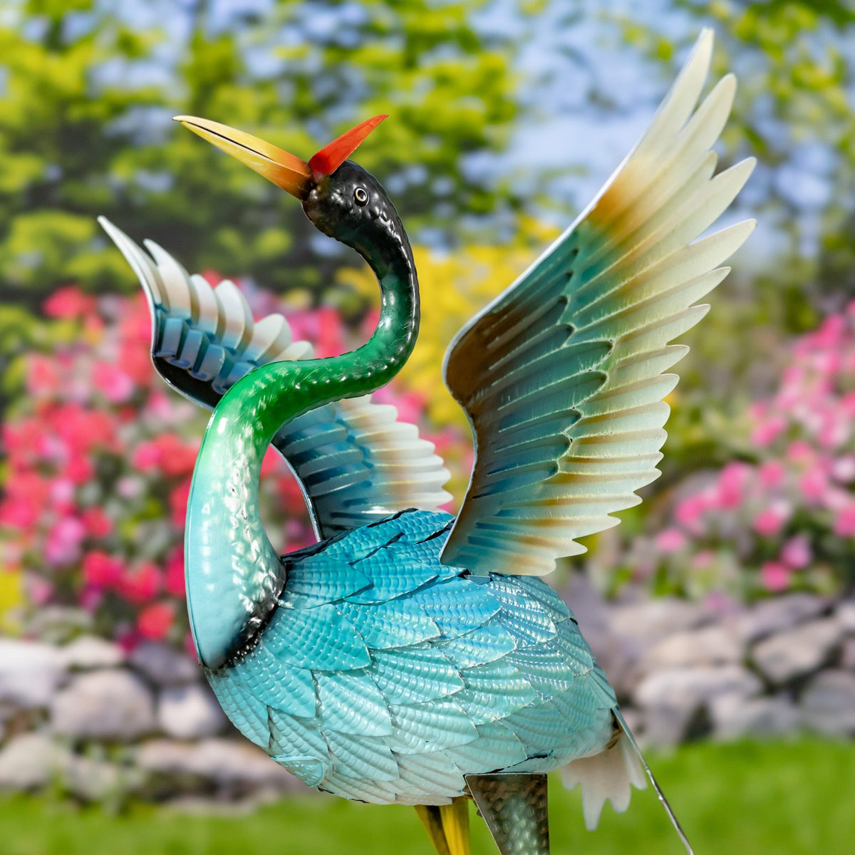 Close view of one blue heron figurine with a curved green neck and raised, pale-tipped wings.
