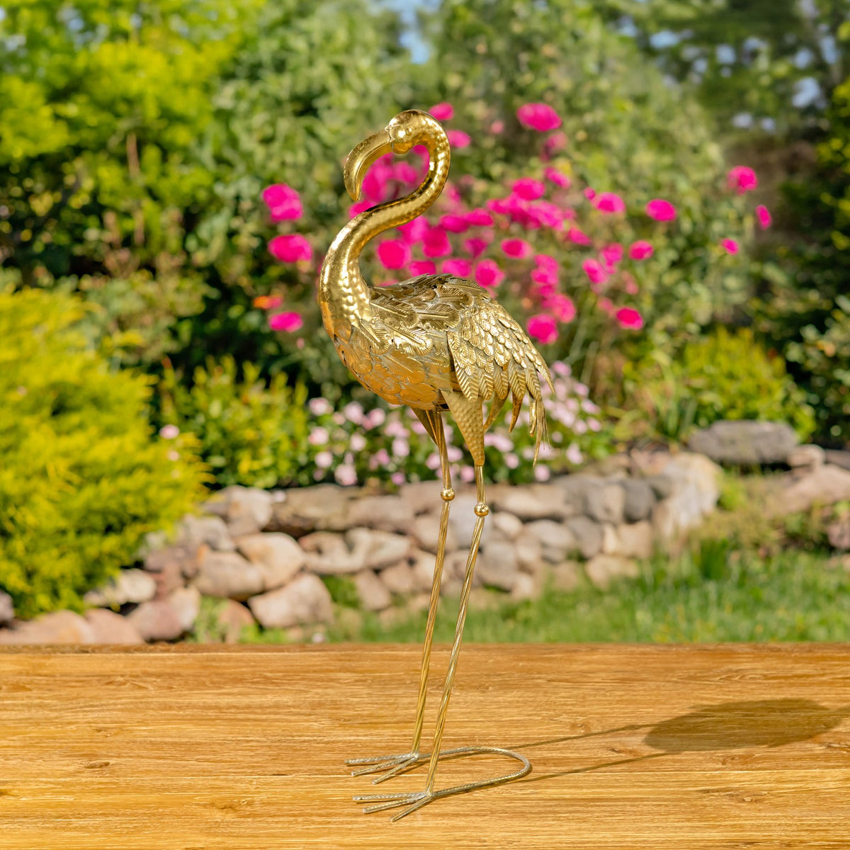 Gold flamingo figurine with folded wings and a curved neck, shown against a garden backdrop.