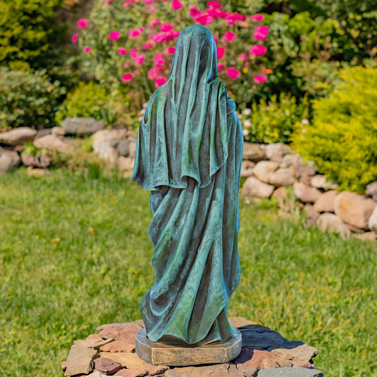 Rear view of the robed statue, showing the draped blue-green veil and gown on a stone garden pedestal.