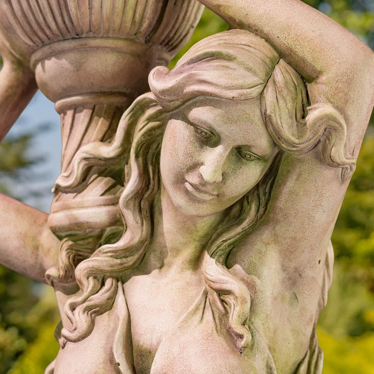 Close-up of the statue’s serene face, wavy hair and raised arm beside the flower pot.