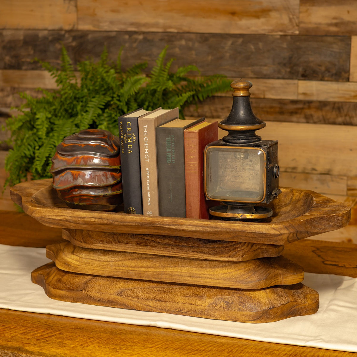 Wooden trays are stacked beneath books, a decorative jar, and a small clock.