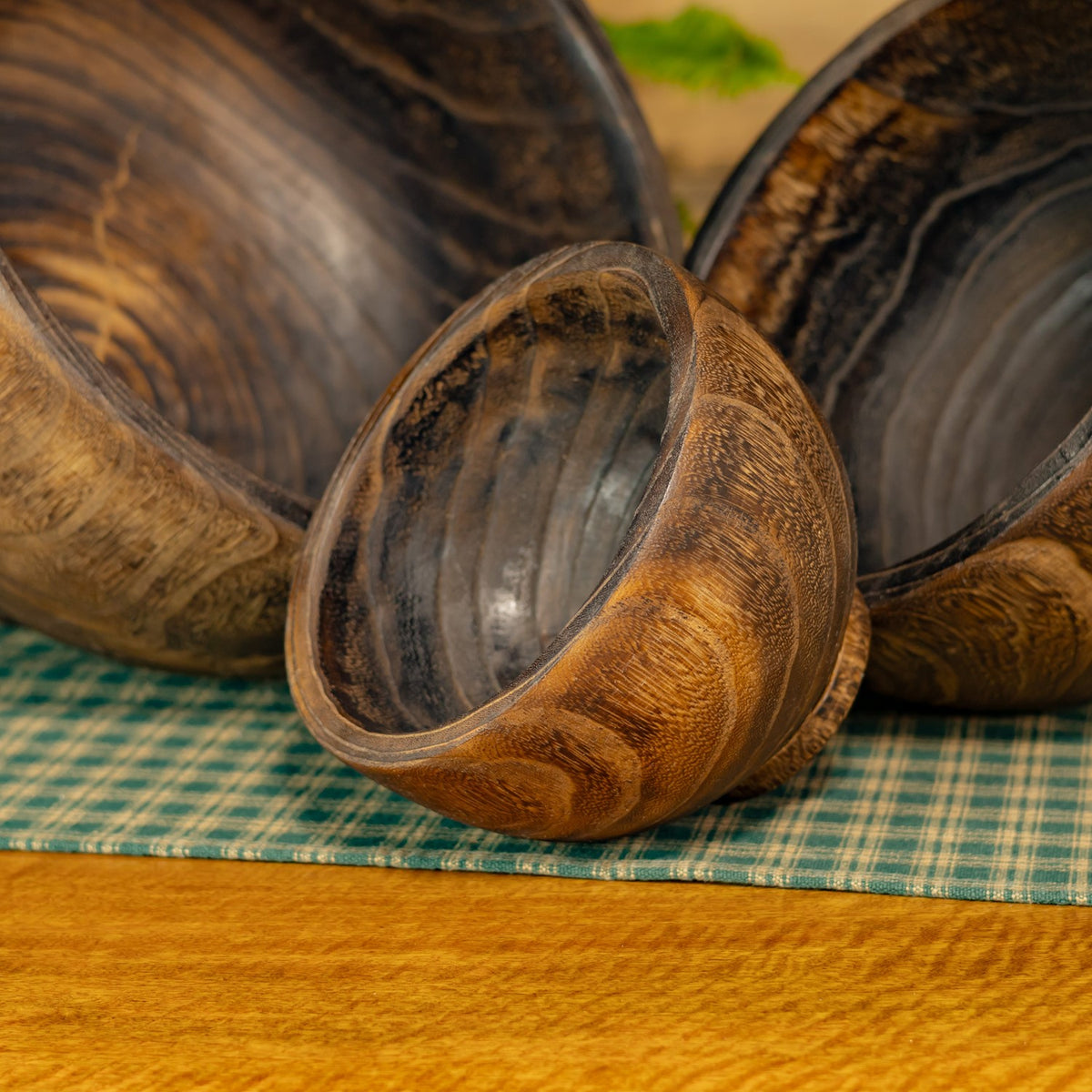 The smallest wooden planter sits in front of two larger bowls, showing their rounded rims and varied grain.
