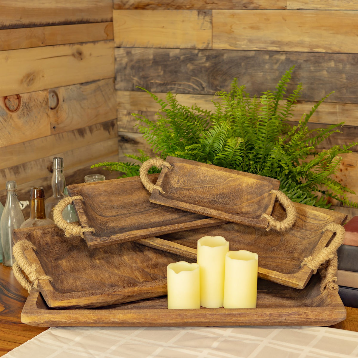 Stacked brown wooden trays with candles and greenery in a rustic setting