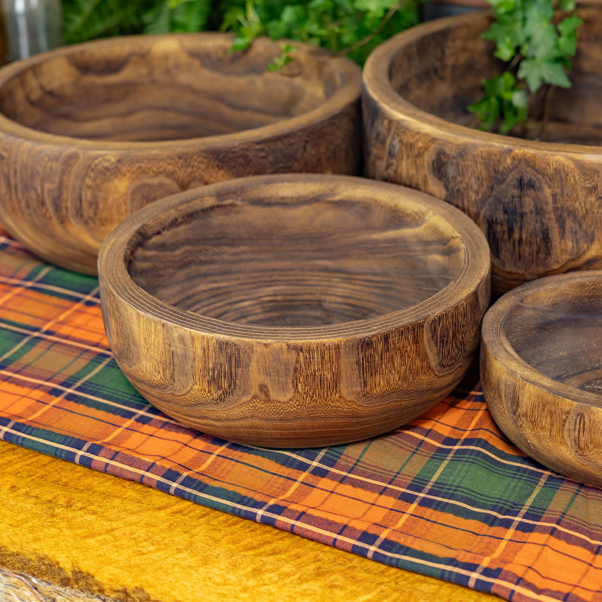 Four round wooden bowls in different sizes arranged together on an orange and green plaid cloth.