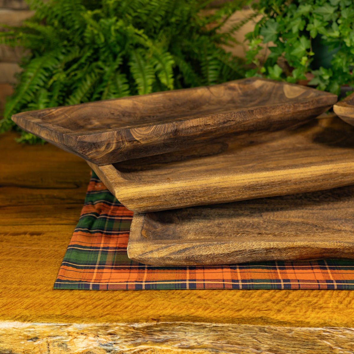 Several empty rectangular wooden trays stacked at staggered angles on a plaid cloth.