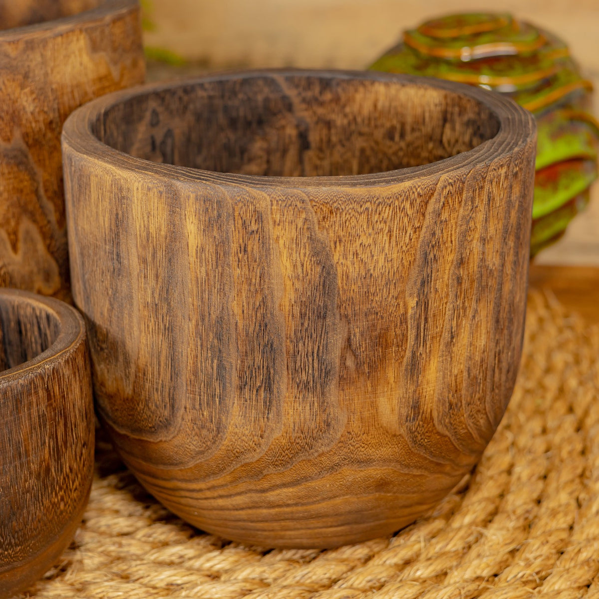 A large wooden bowl sits on a woven mat, with dark streaks running through its grain.