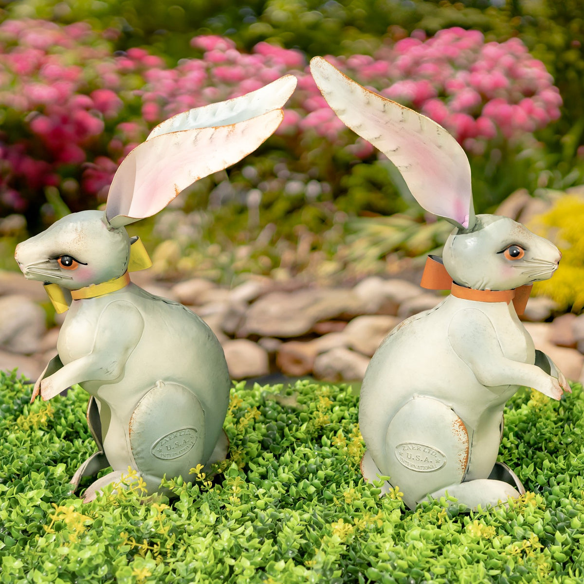 Two pale metal rabbit figurines shown in profile, each wearing a different colored neck ribbon.