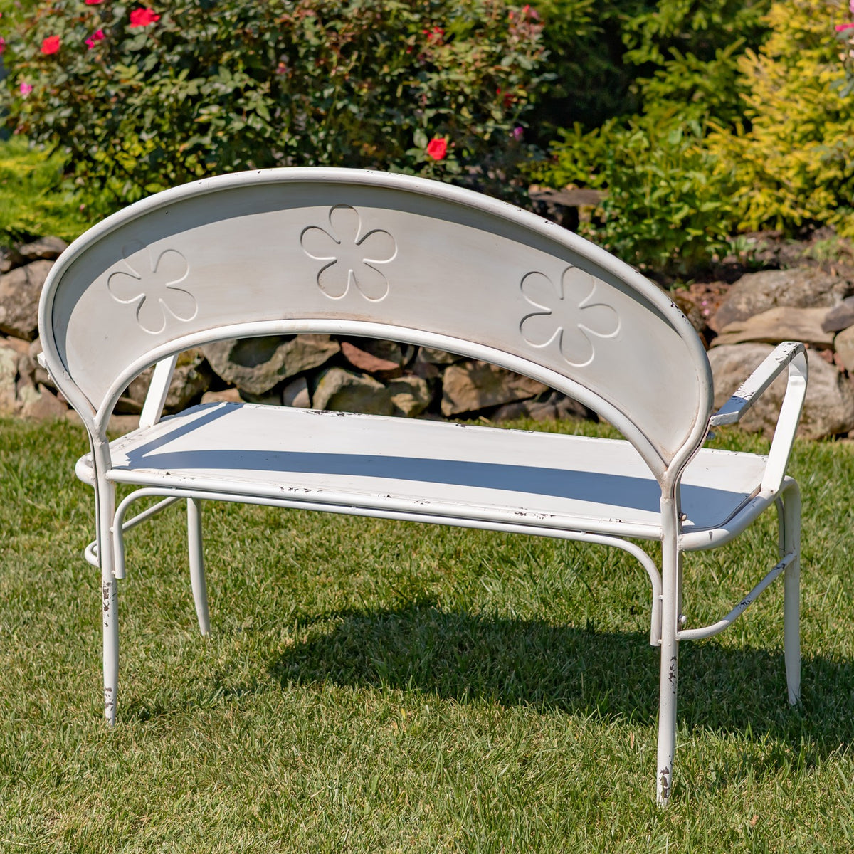White garden bench on grass, shown from behind with three flower-shaped cutouts in its curved backrest.