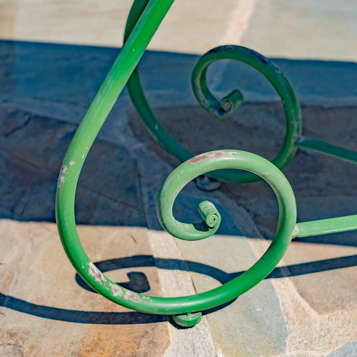 Close-up of a green iron leg’s curled scrollwork, showing worn patches in the finish.