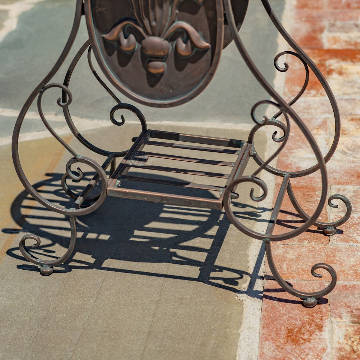 Close view of a scrollwork metal stand with a rectangular slatted platform and decorative oval panel.