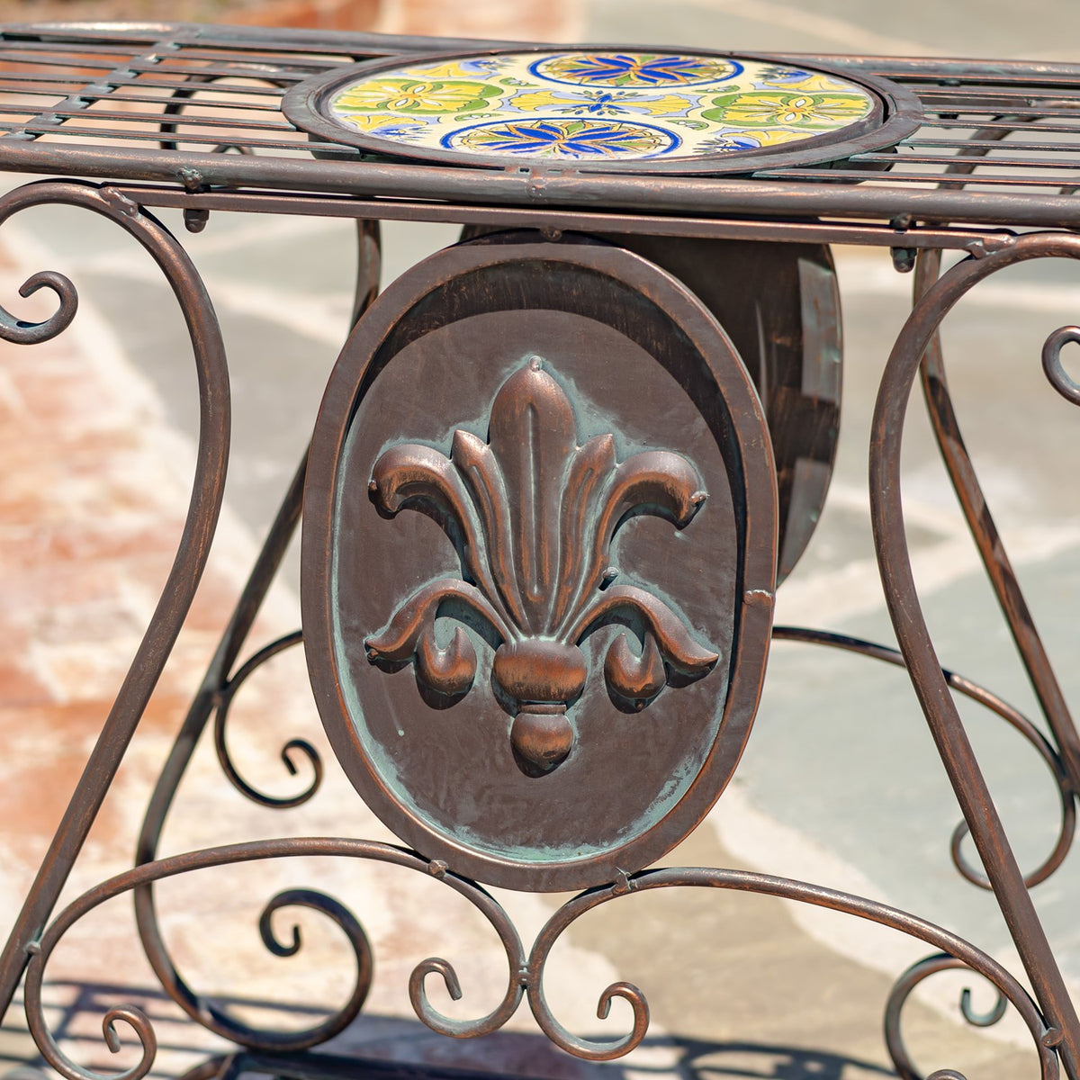 Colorful circular mosaic top above an oval metal panel with a raised floral motif.