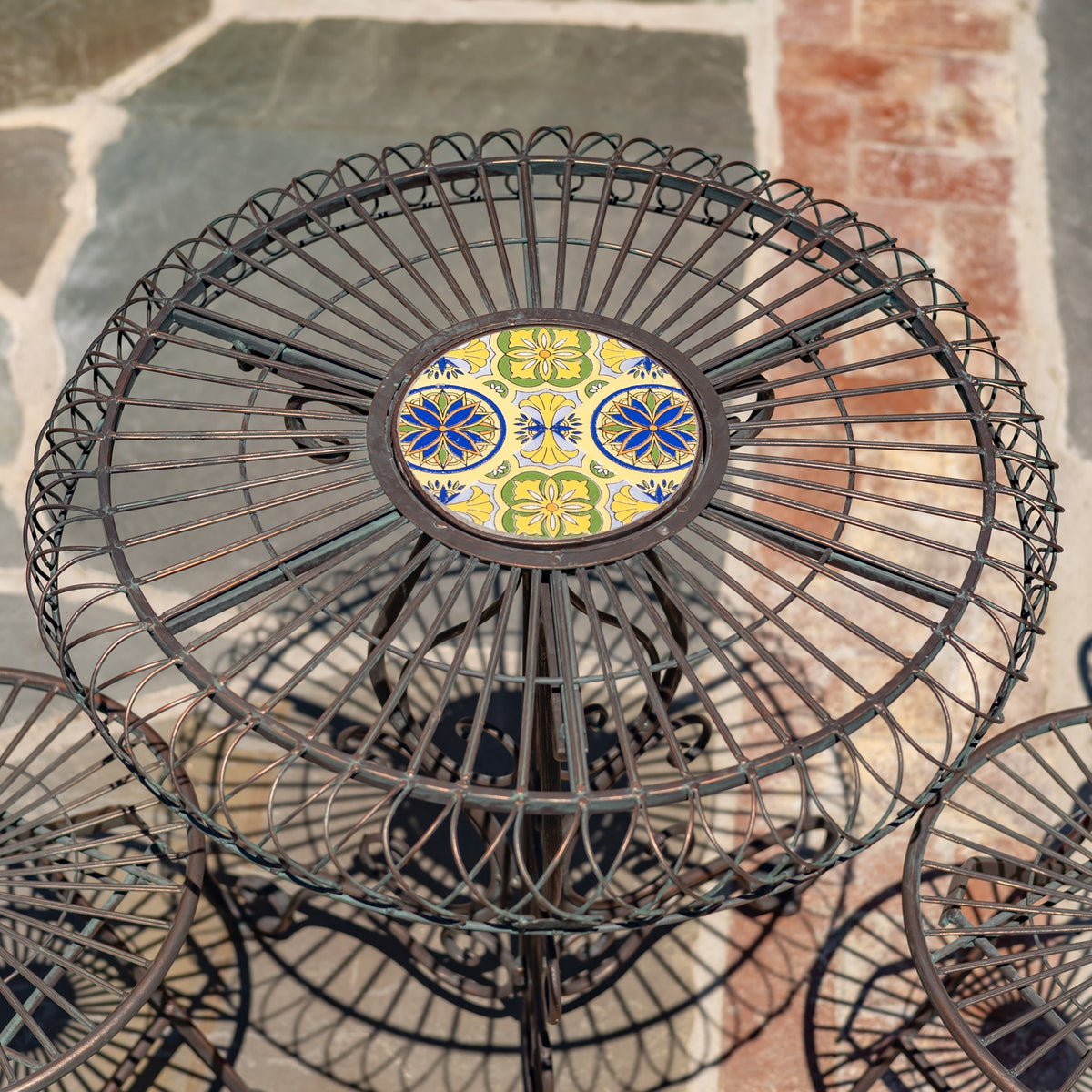 Overhead close-up of a round wire table with a colorful floral mosaic tile at its center.