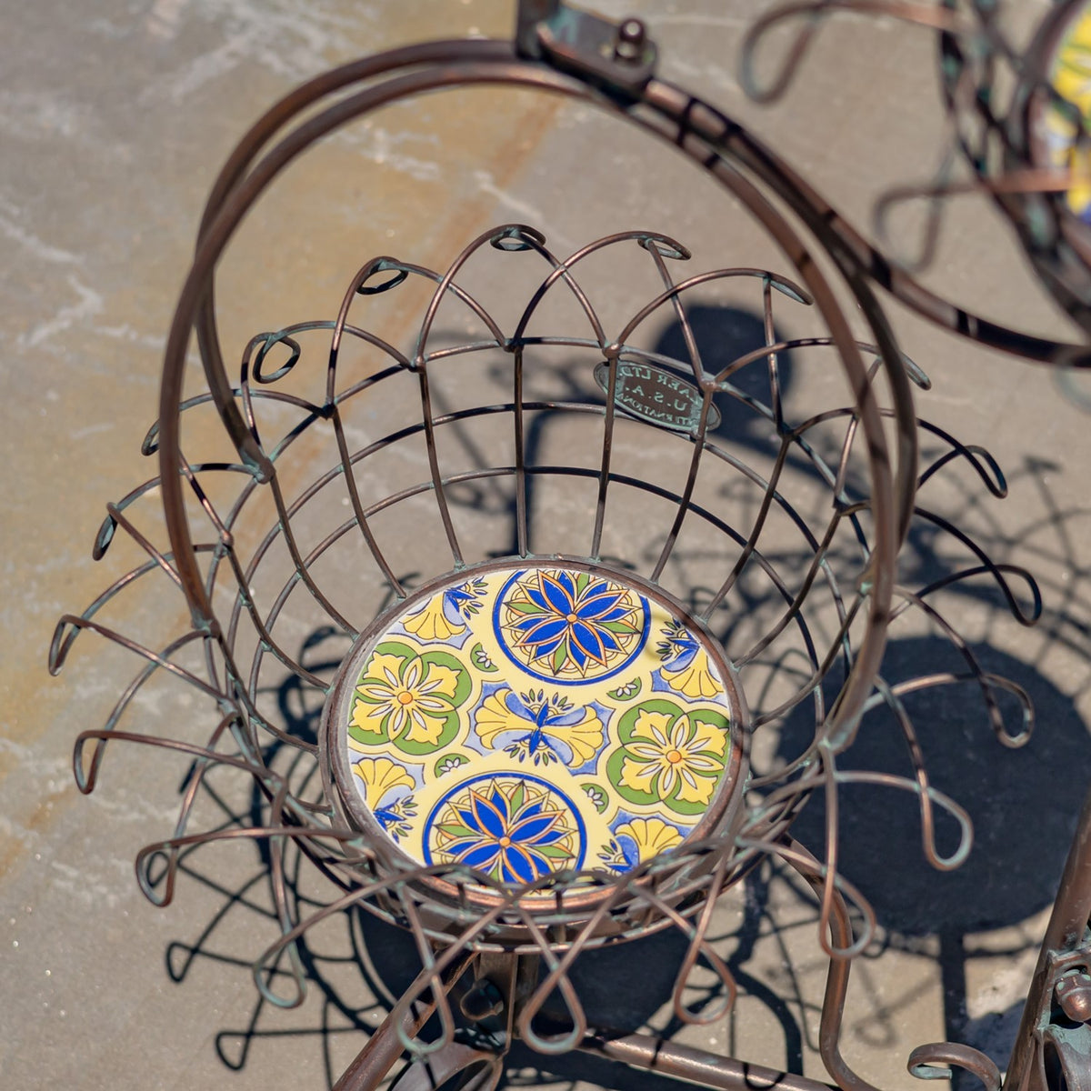 A round wire basket with curled edges surrounds a colorful patterned ceramic base.