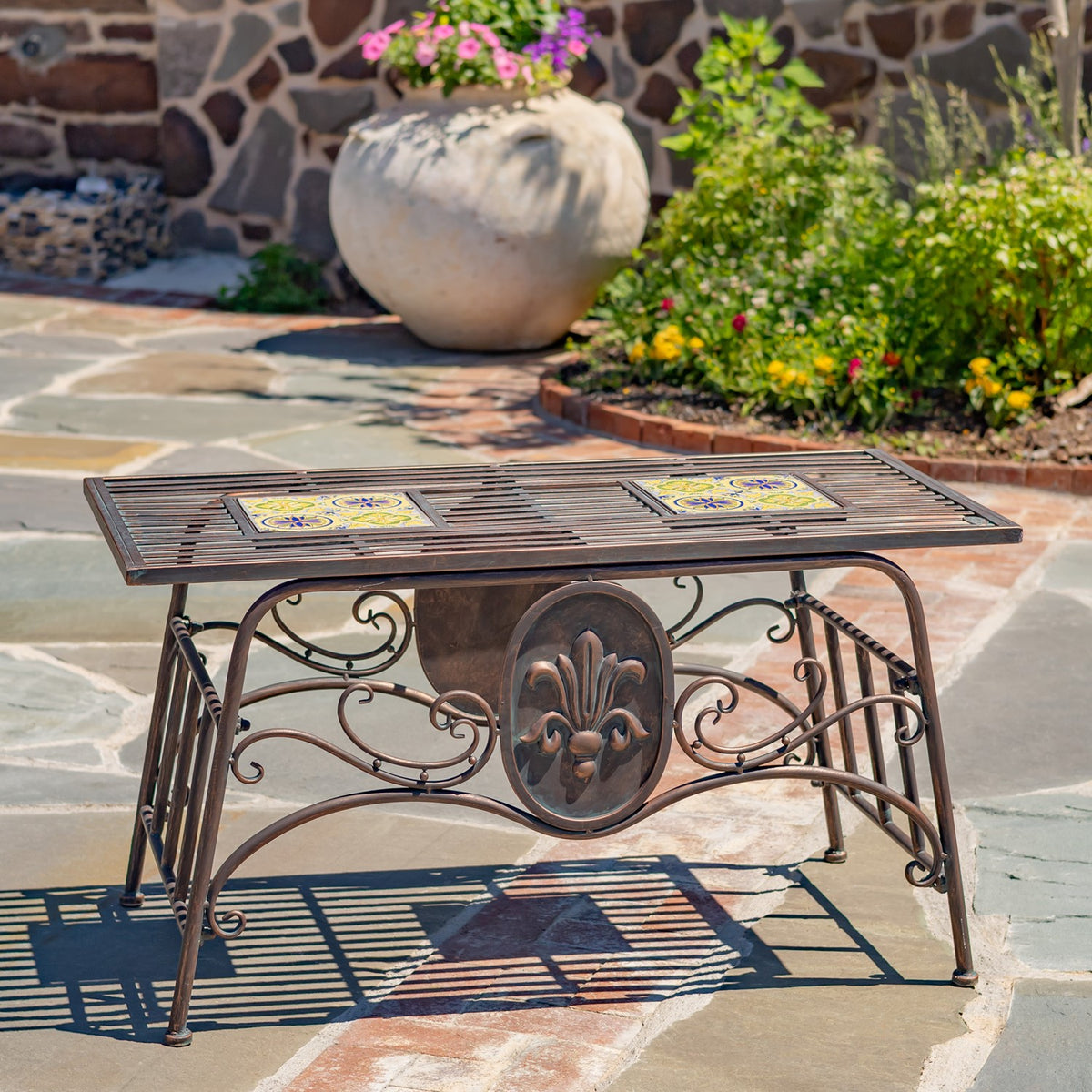 Rectangular metal table with two colorful mosaic panels, ornate scrollwork legs, and a central fleur-de-lis medallion.