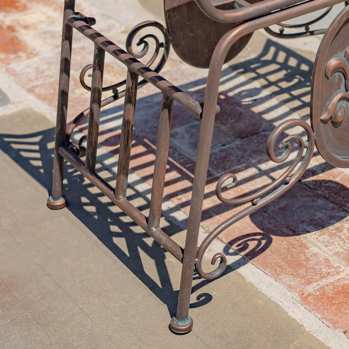 Close view of the chair’s metal legs and curled side scrollwork casting shadows on stone paving.